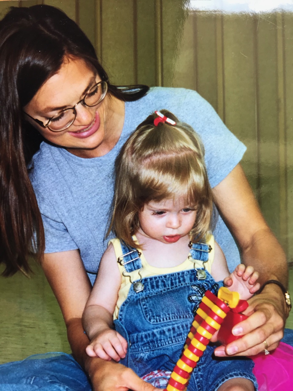 Caregiver holding a toddler in her lap while engaged with a yellow and red instrument
