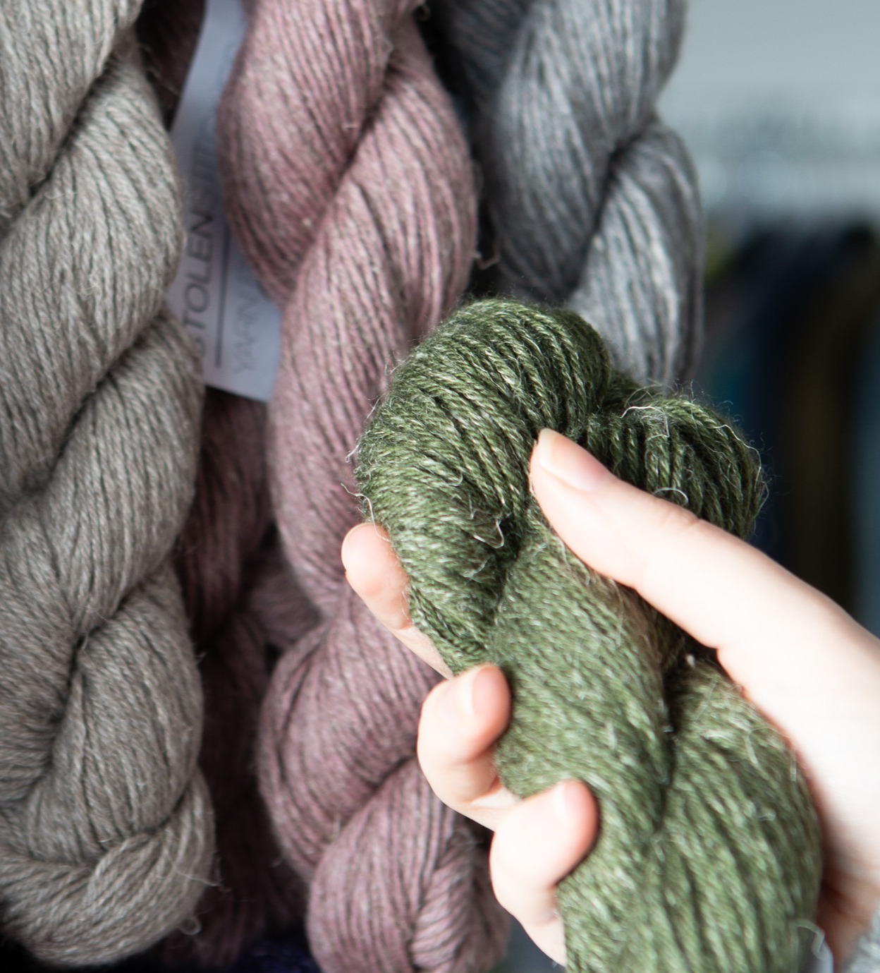 A hand holding a skein of green yarn up to a skein of pink yarn. 