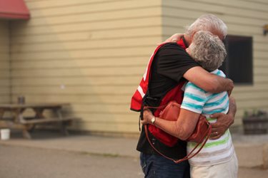 Two people are hugging in front of a picnic spot. One is a Canadian Red Cross volunteer wearing a Red Cross vest. 