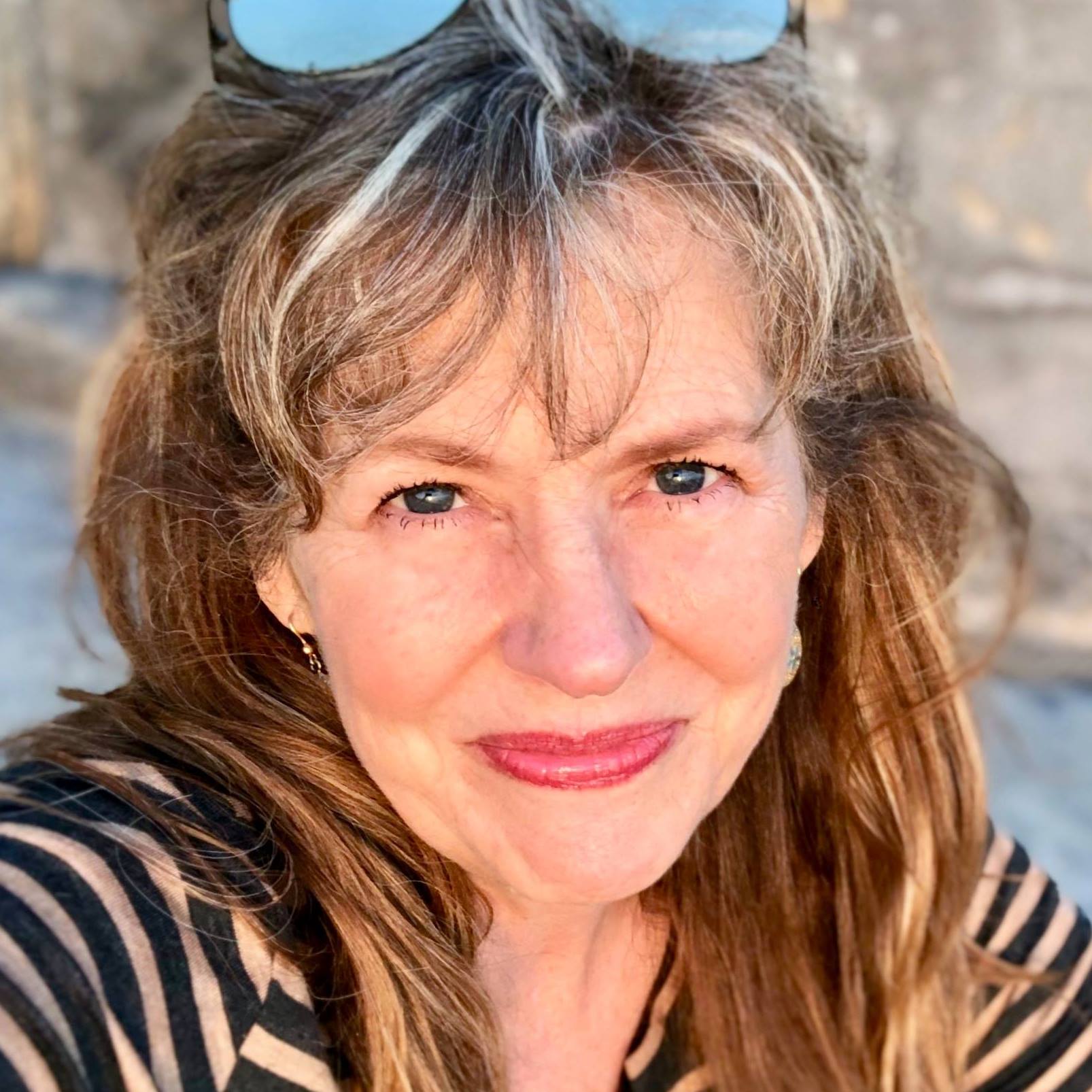 A picture of Allison. She is a white woman with brown graying hair and dark pink lipstick. She is wearing a black and white striped shirt and looking up into the camera.