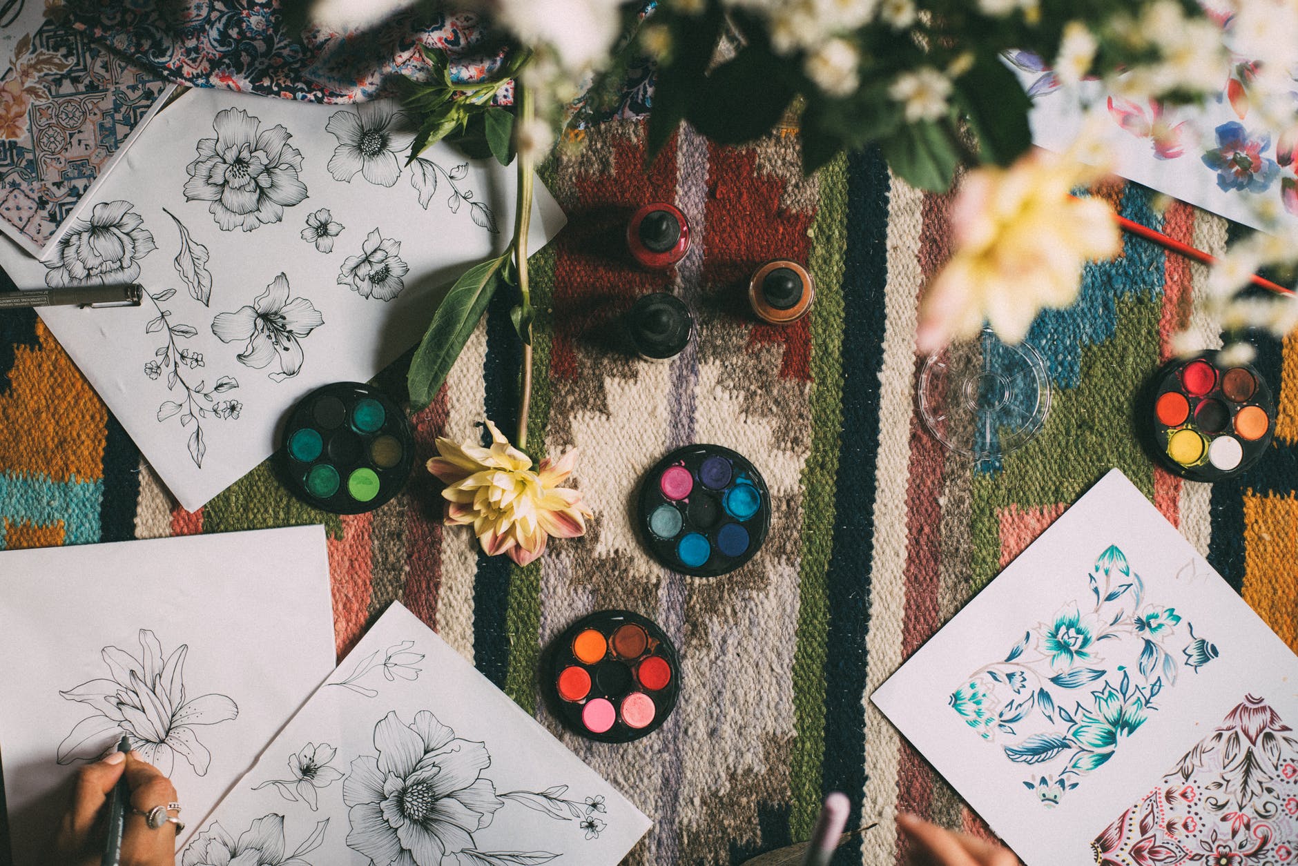 several drawings of flowers and paints layed out on a colourful table