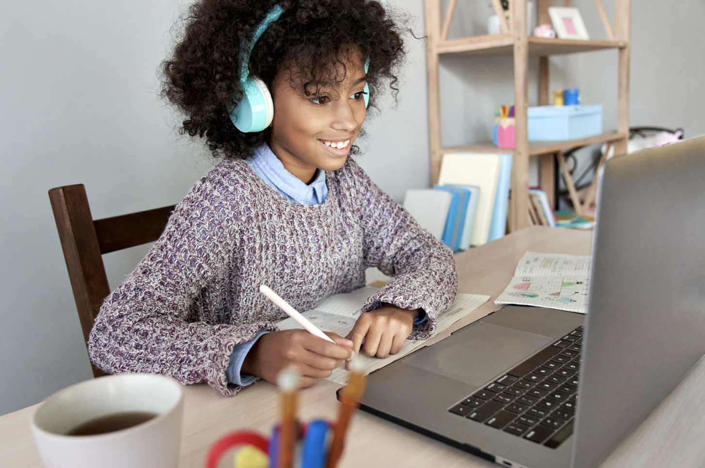 A young girl sits in front of a laptop, taking notes.