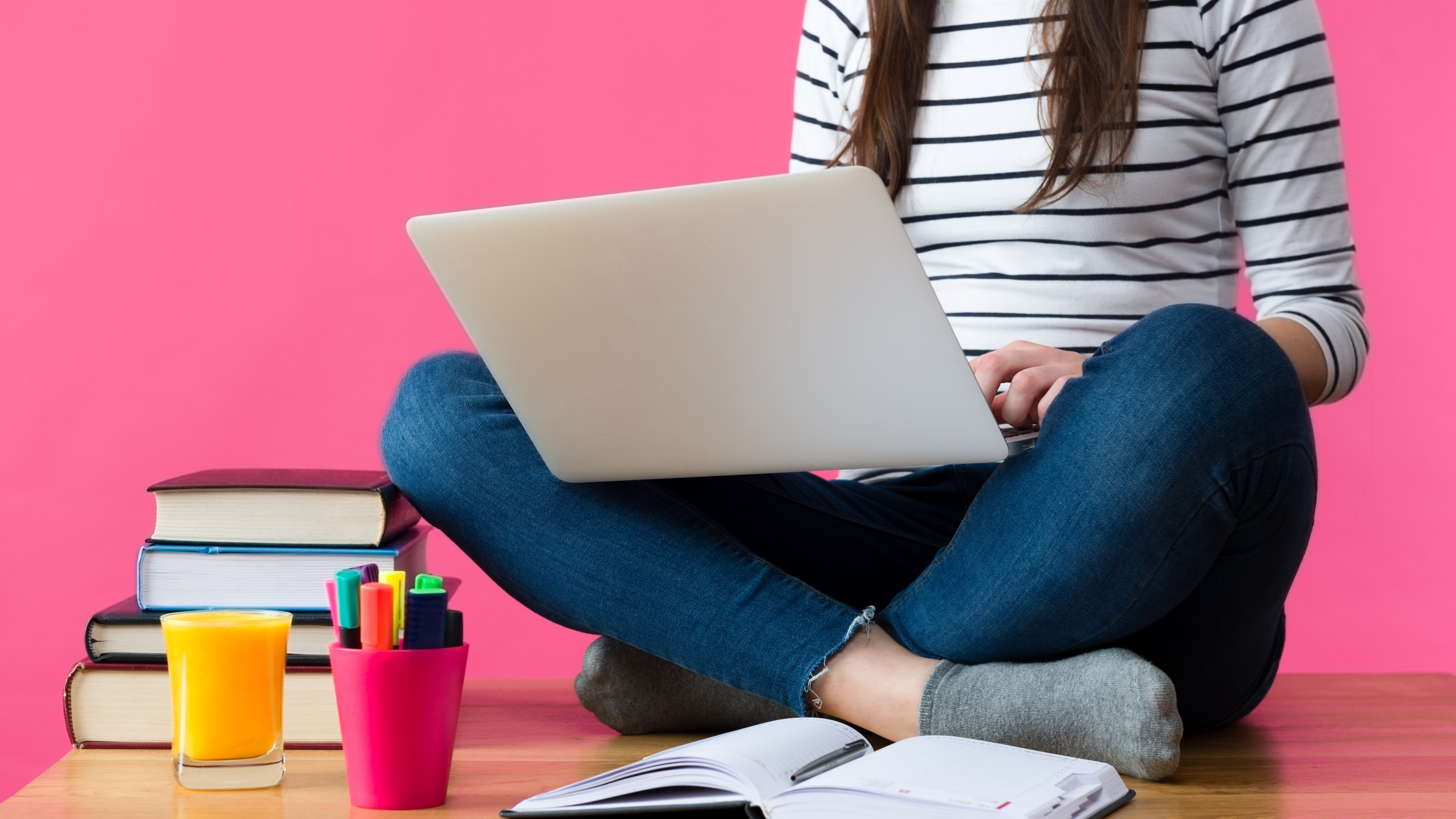 woman sitting cross-legged on floor with open laptop and books and pencils