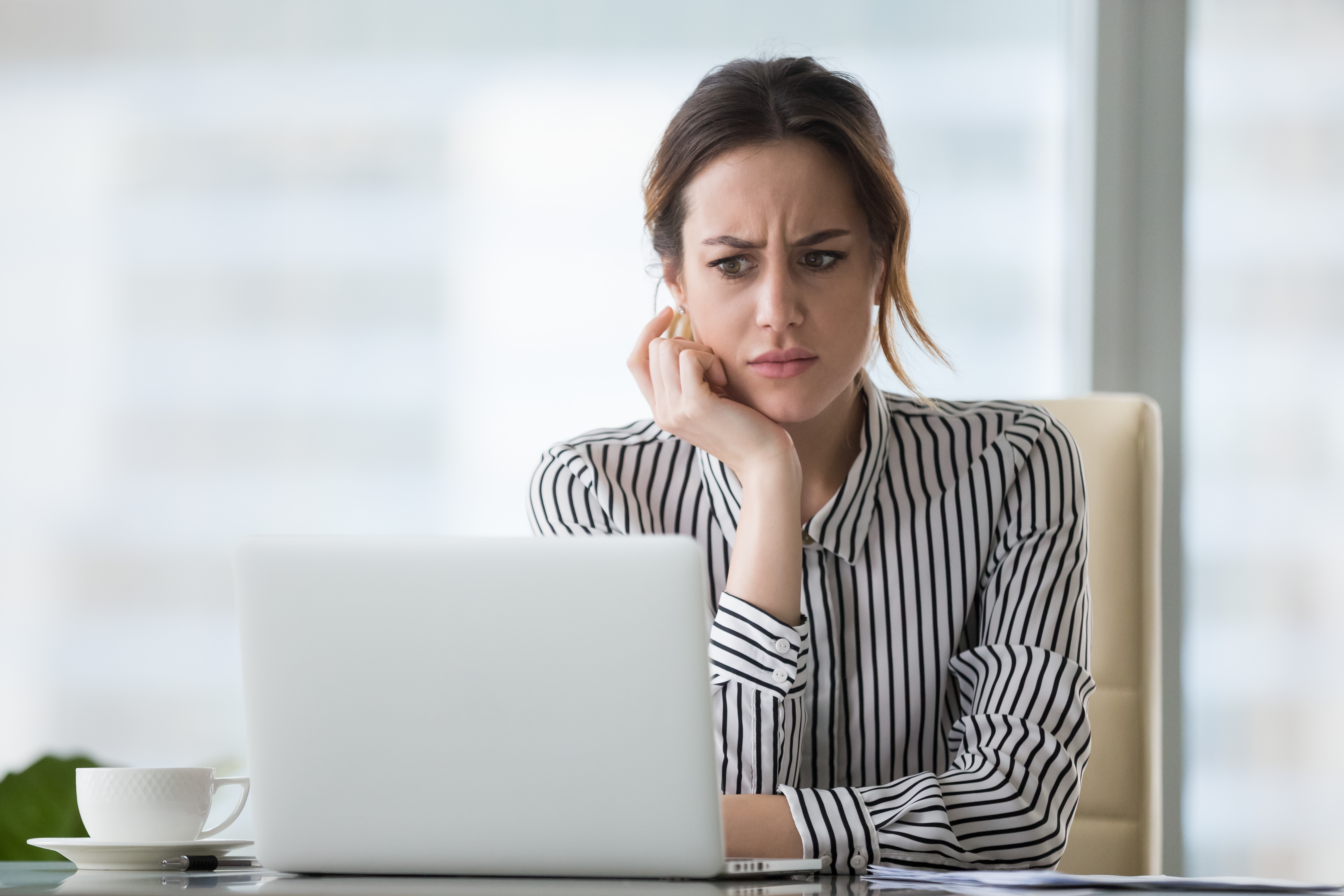 Young professional white woman looking at a laptop screen with a confused expression