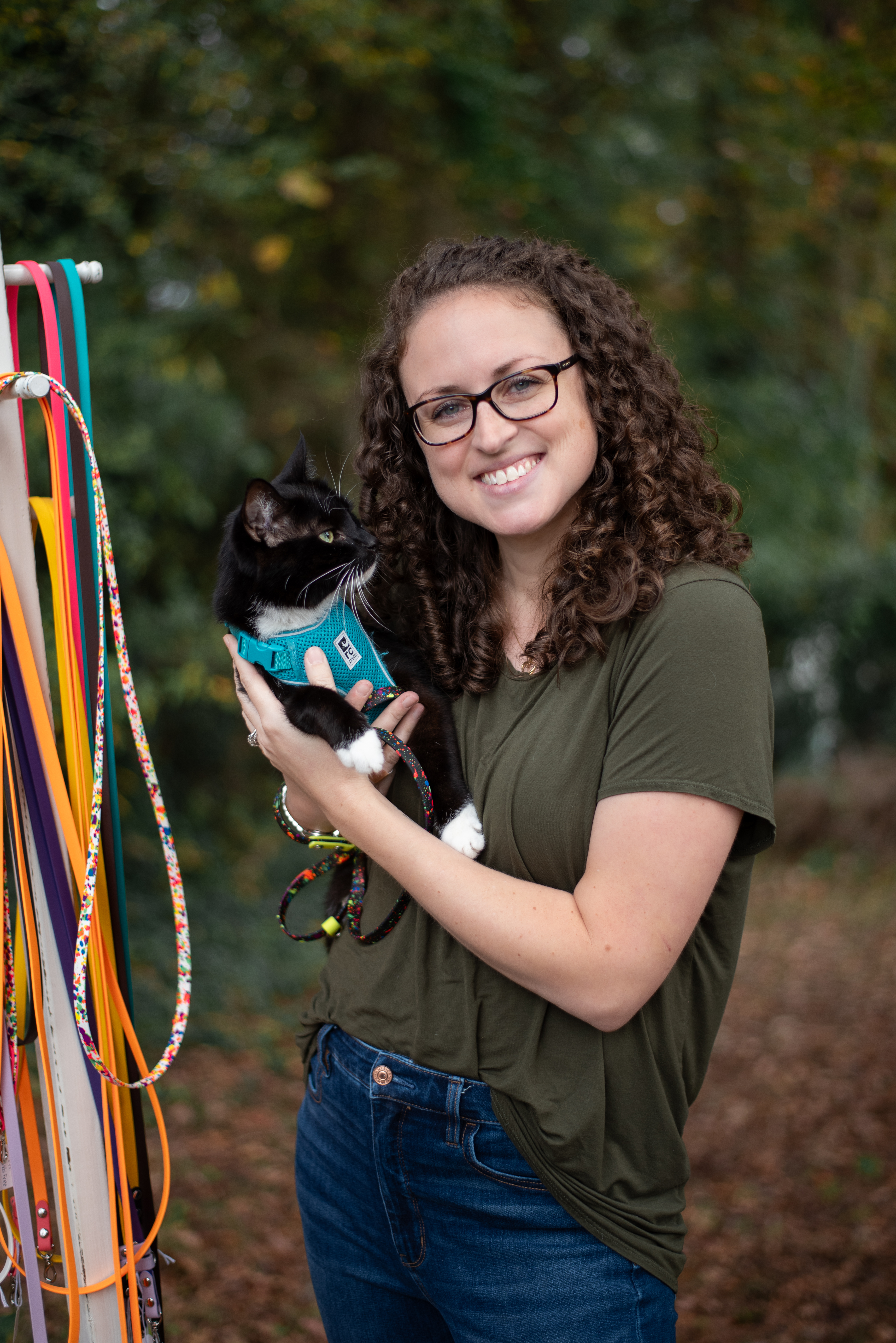 woman standing outside holding a cat on a harness and leash