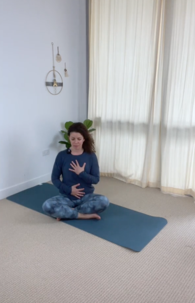 Female teacher seated cross legged with hands on her torso