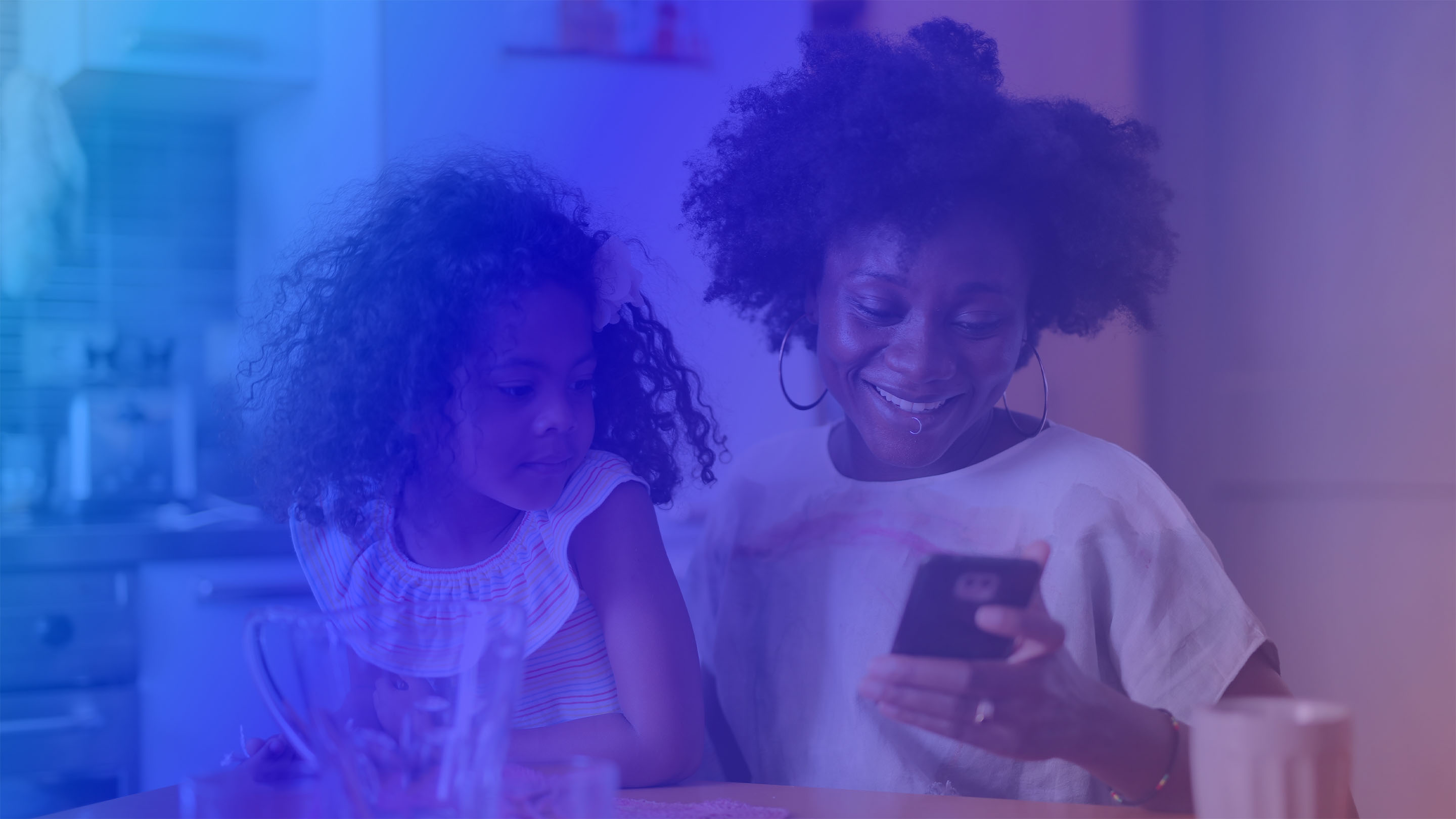 a woman smiles while holding her child and looking at her smartphone after finding student loan relief