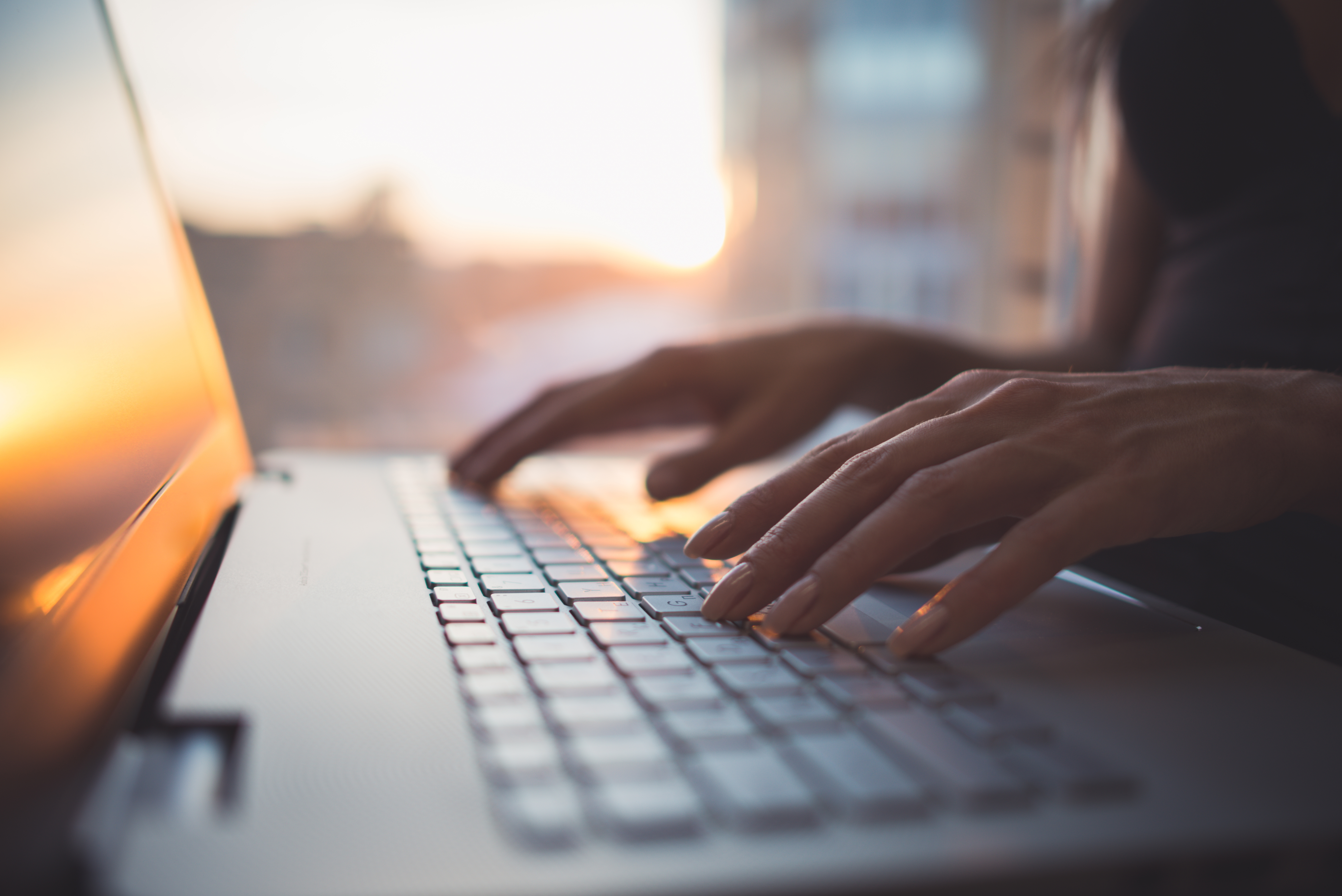 Image of hands typing on a laptop lit by a sunset