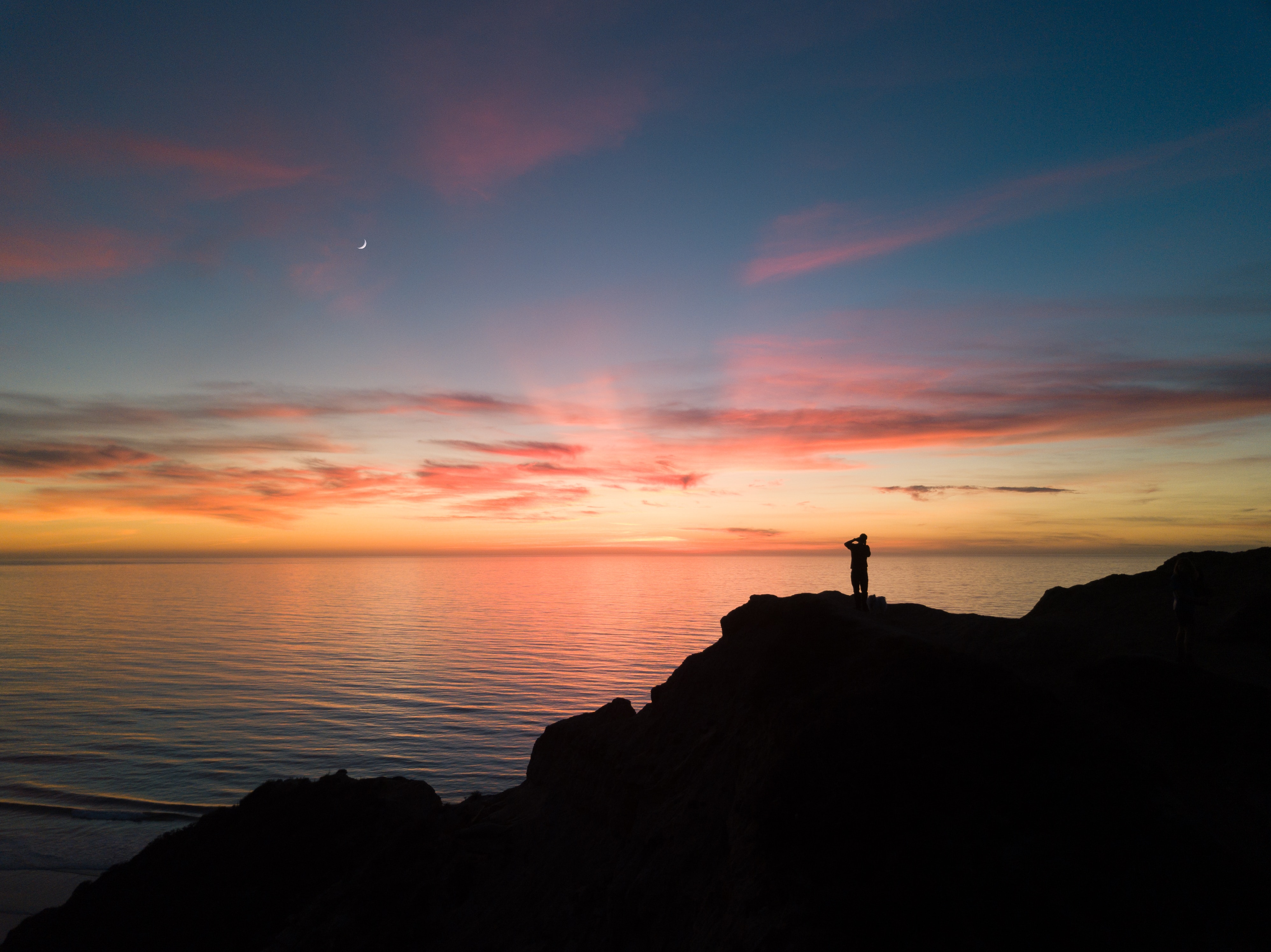 A man stands on a cliff at sunset