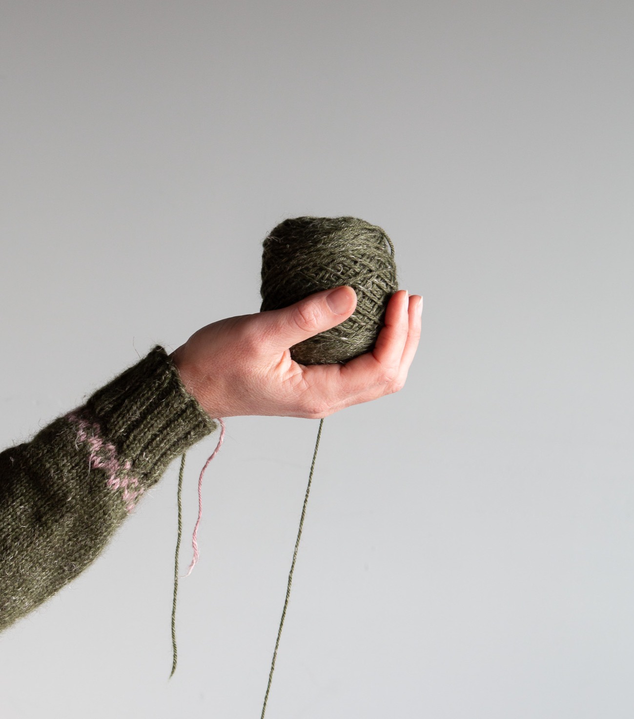 Hand holding a ball of wound Nua Sport yarn in a green shade. 