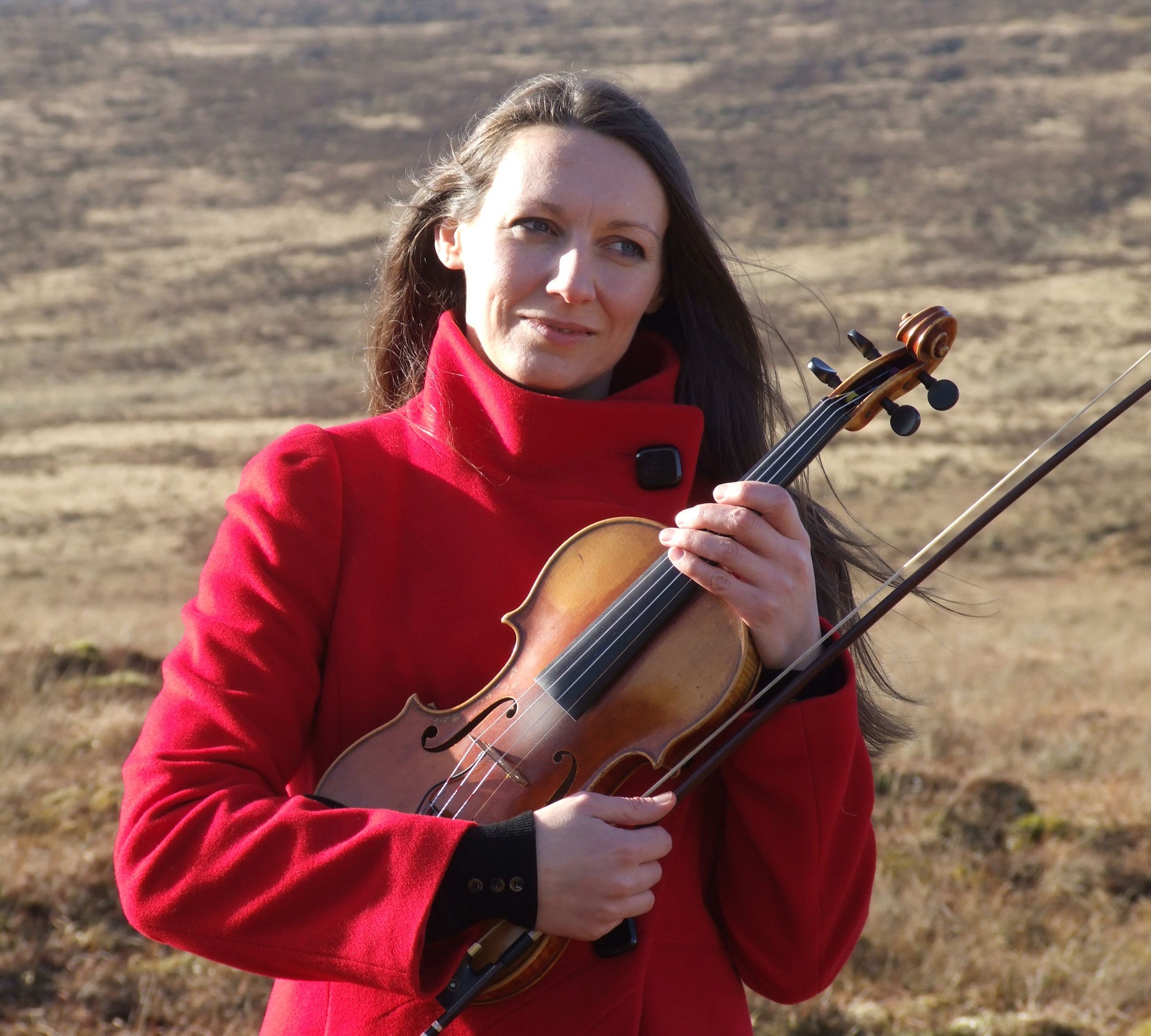 Profile shot of Theresa Kavanagh Holding her Fiddle with grassland background.