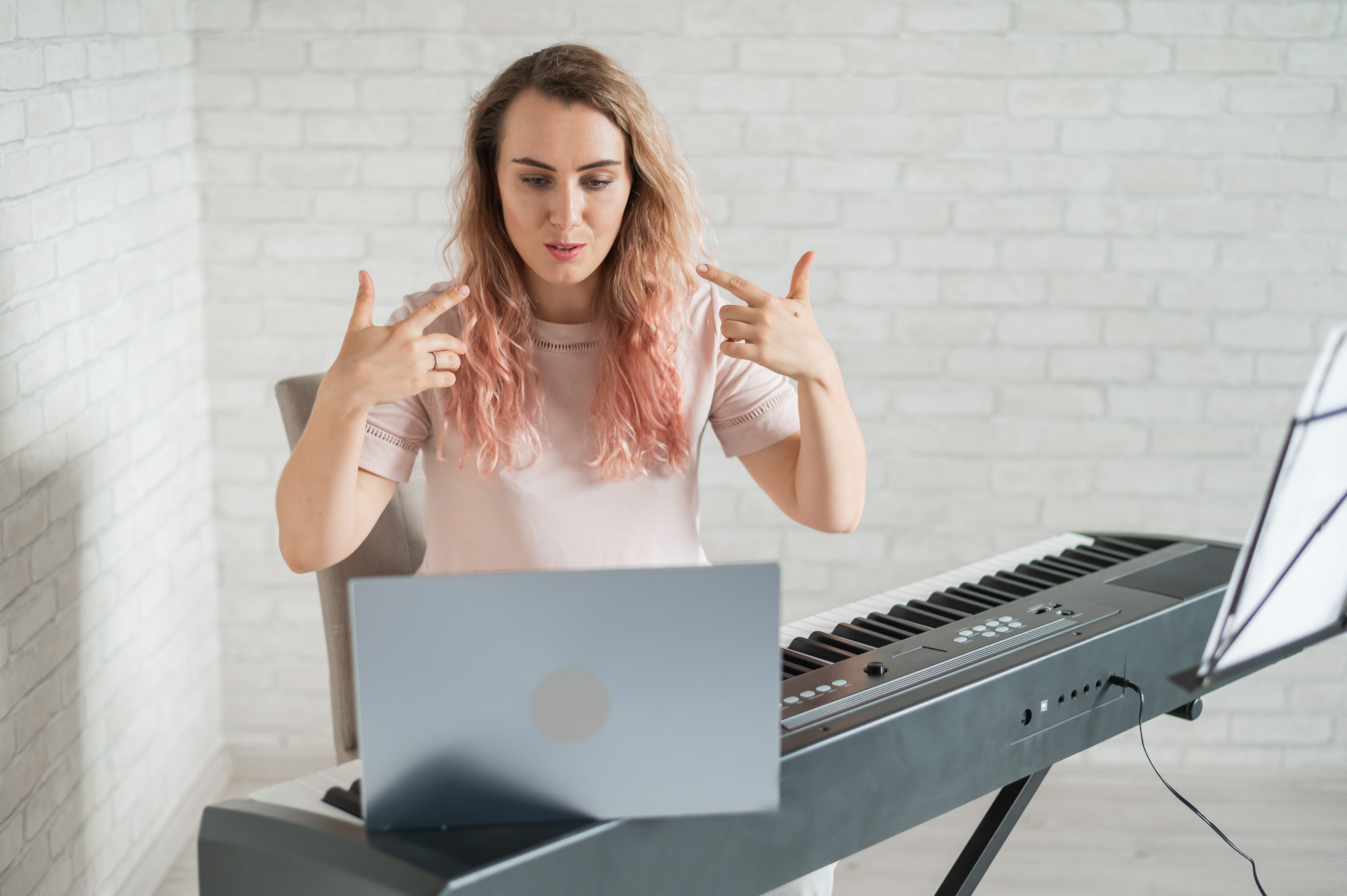 singing teacher sitting at a keyboard with a laptop giving a singing lesson on the internet