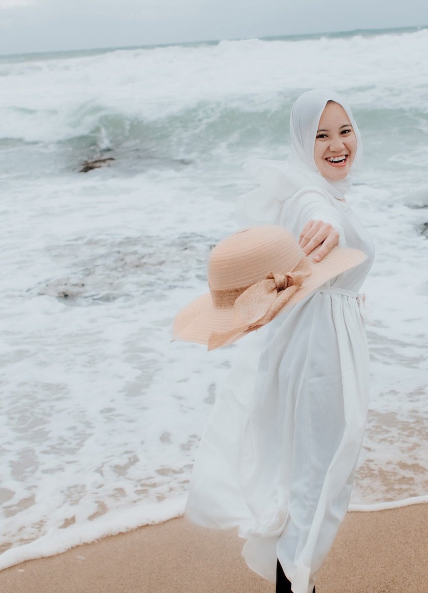 laughing hijabi on beach holding pink hat