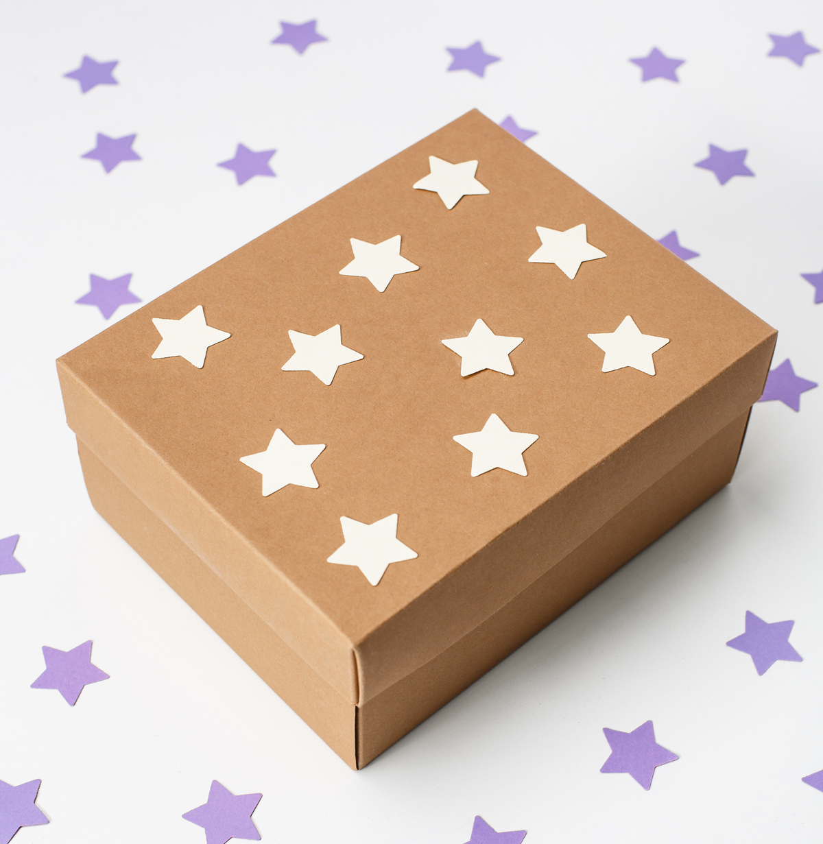 A brown box covered in white stars, sitting on a white table covered in purple stars