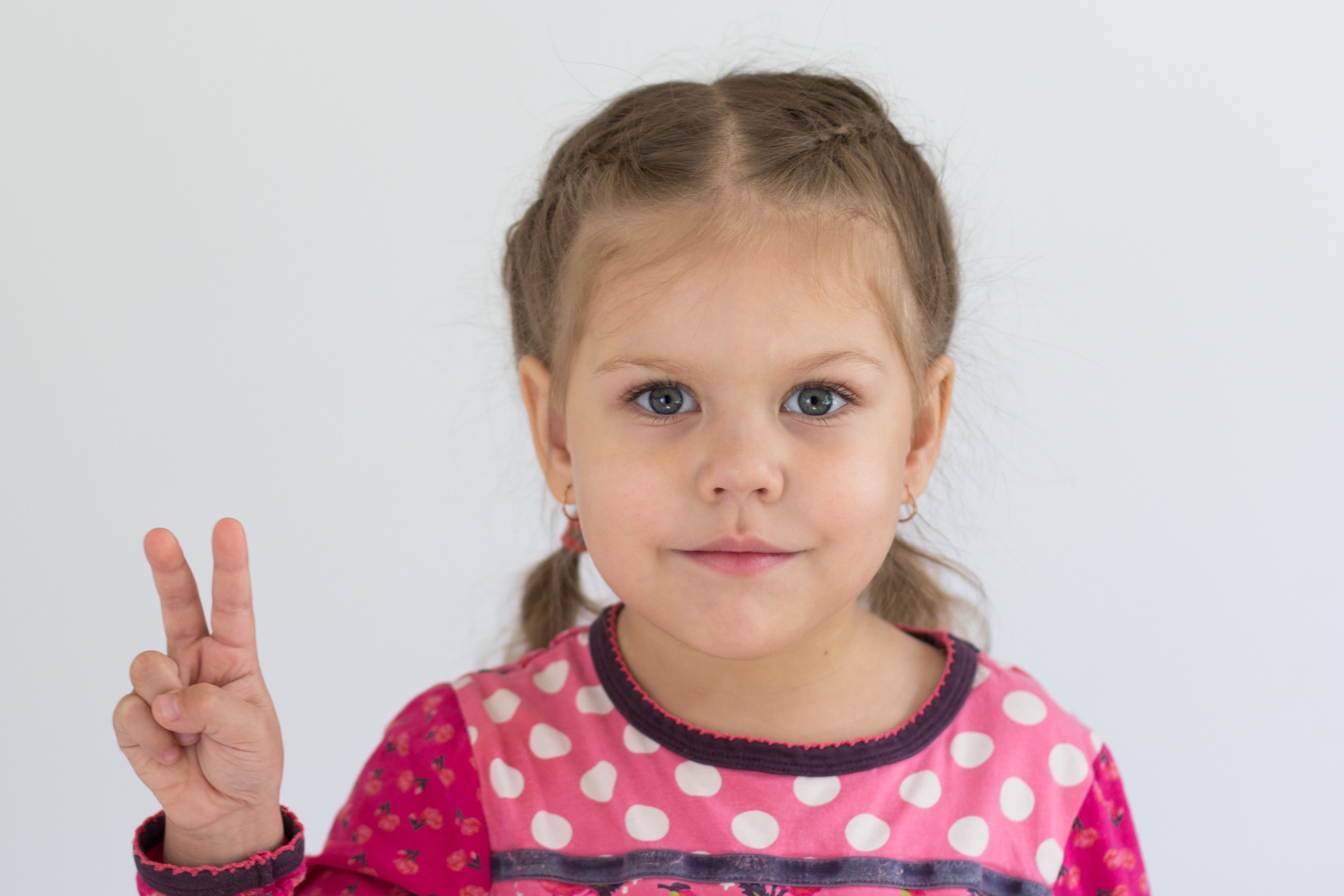 a little girl in pigtails wearing a pink shirt holding up two fingers