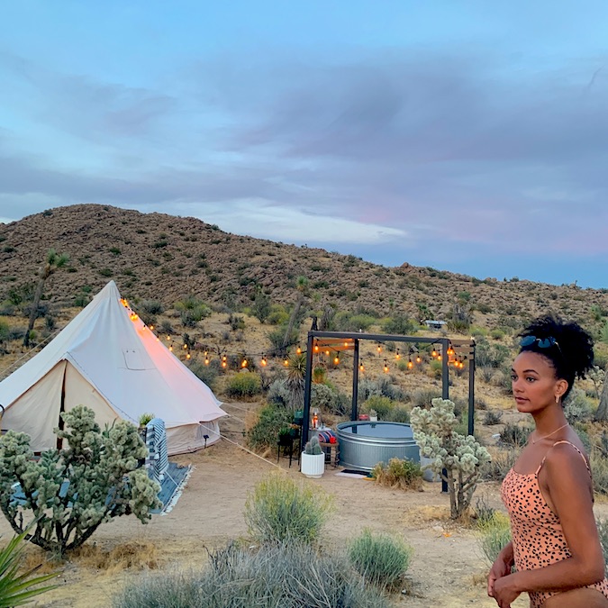 Black woman standing in her swimsuit at a desert glamping campsite with a steel basin for a pool