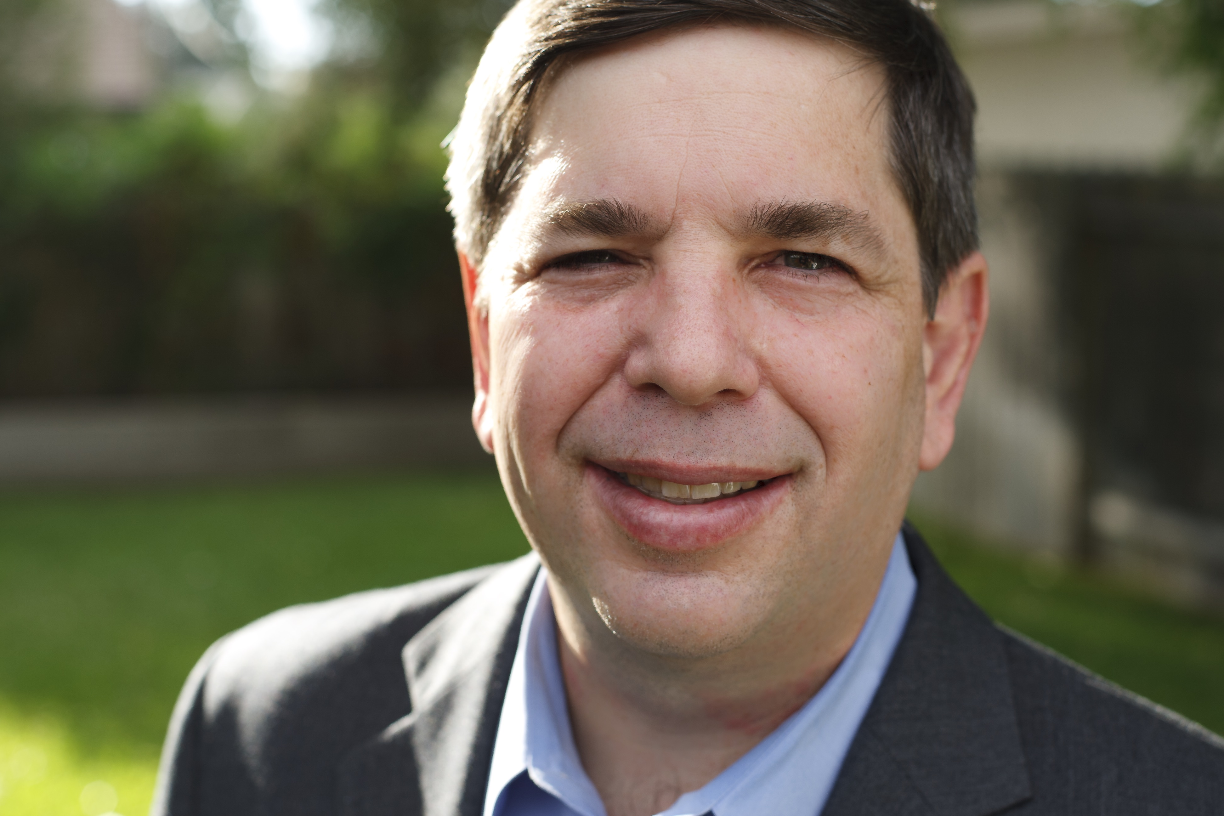 Close-up photo of David Sparks outside, smiling, wearing a gray sports jacket and light blue shirt.