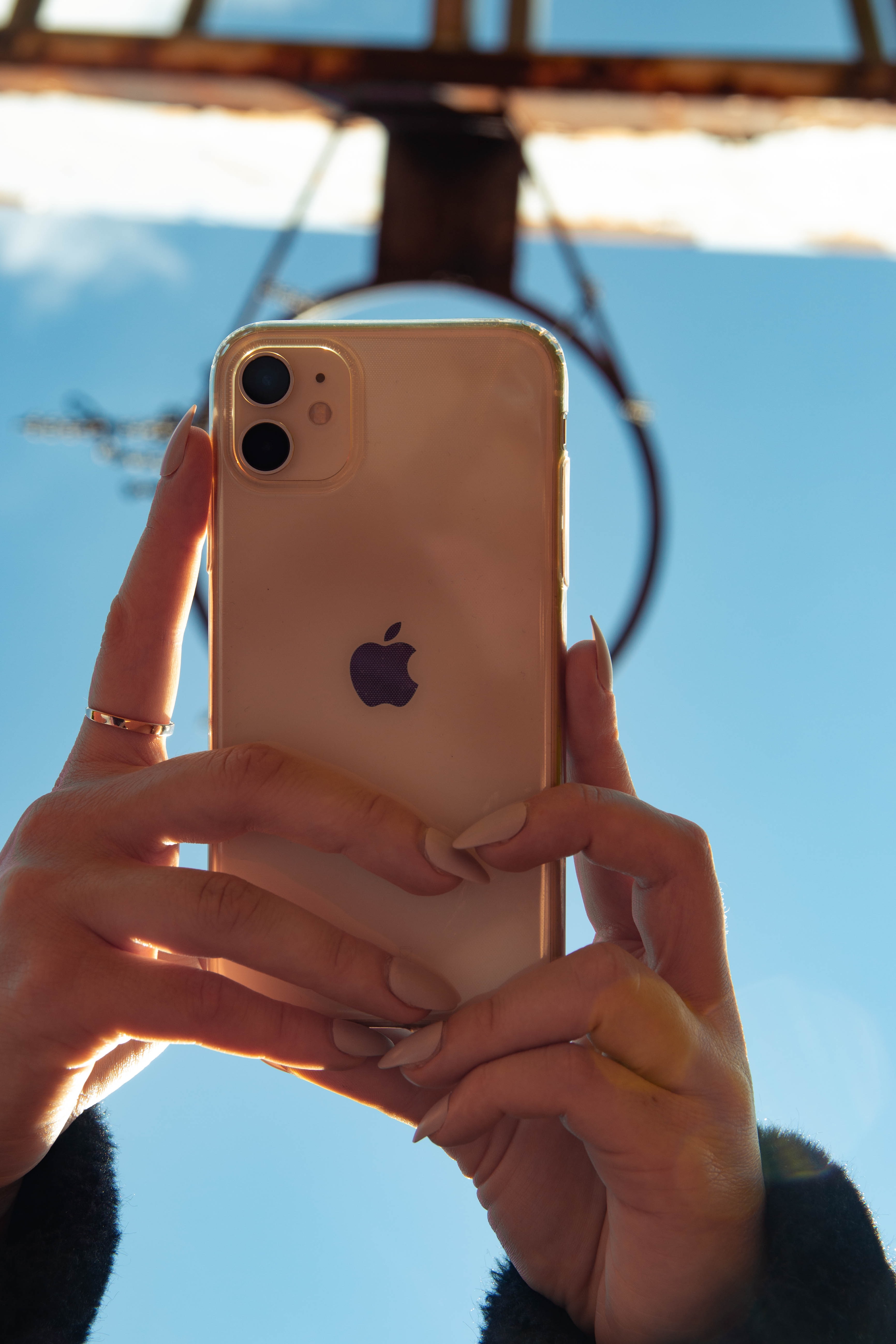 Hands holding an iPhone to take a picture of the sky and a basketball hoop.