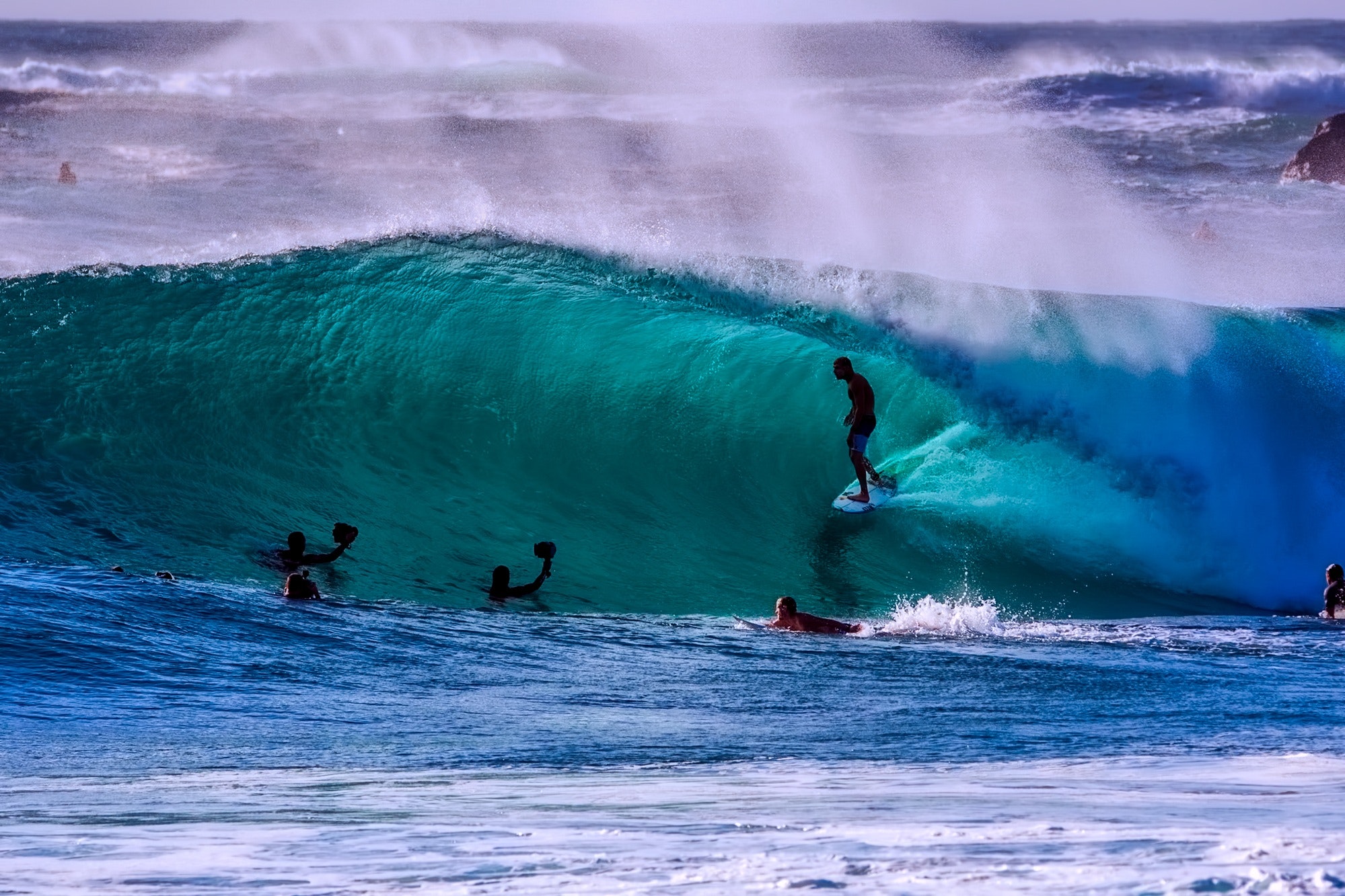 Surfer riding a wave with other surfers and photographers in the water