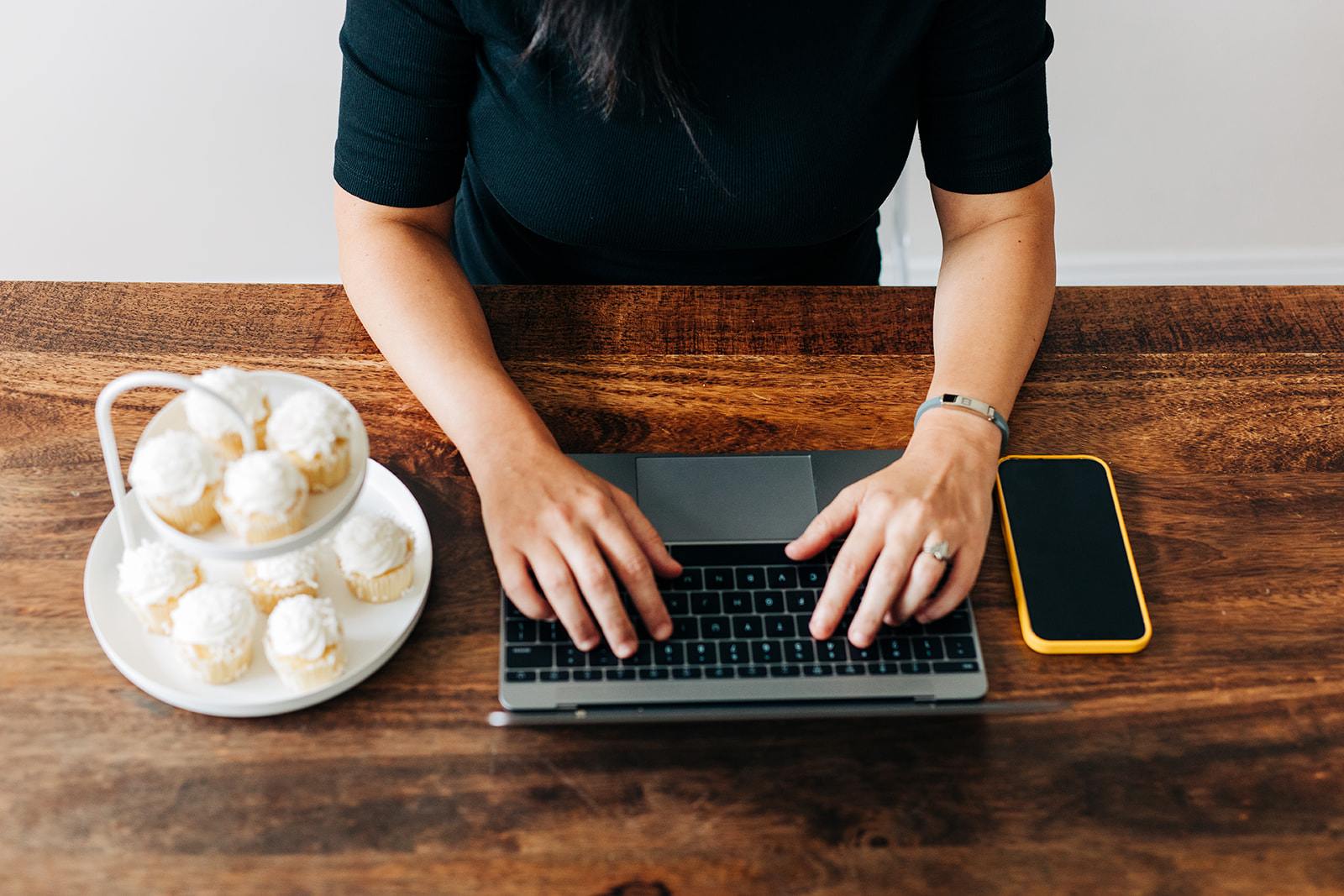 Birds eye view of a wood desk with a macbook, a green glass filled with water, a white mug filled with coffee and a textured dark green water cup with a lid and a straw.