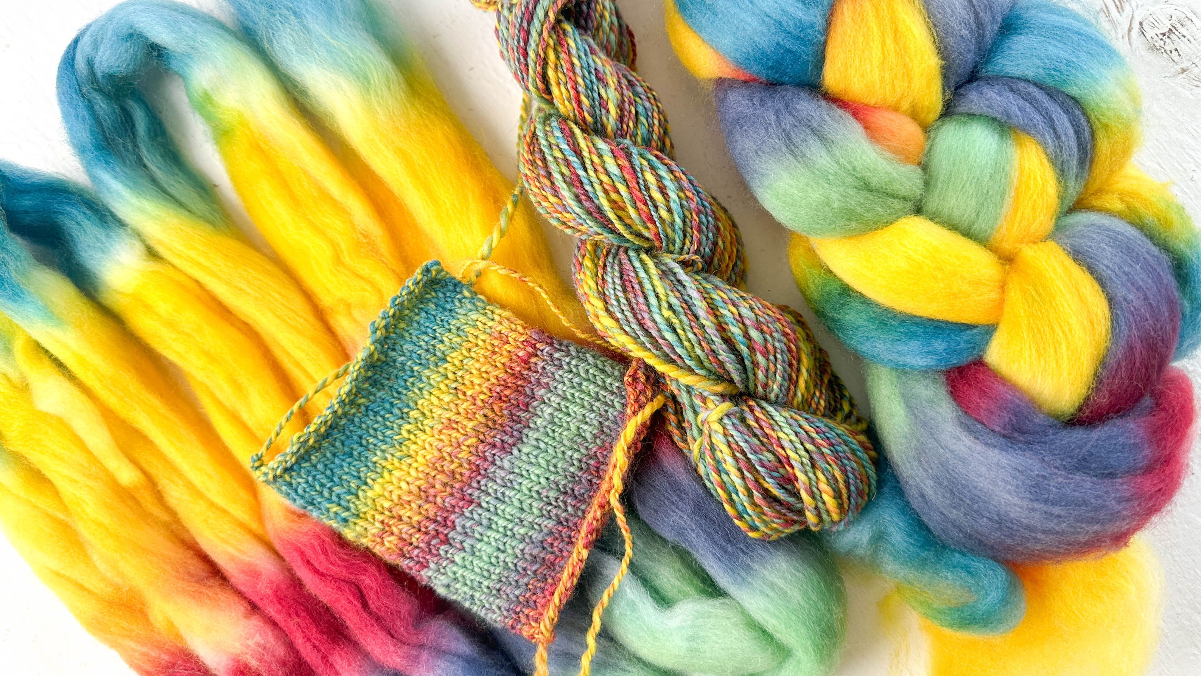 A selection of wool roving, handspun yarn twist, and a knitted swatch highlighting color variations, the roving is in bright yellow, pink, purple, and blues