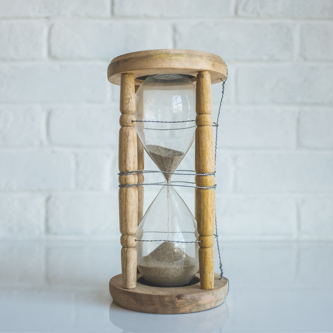 Wooden sand timer against a white brick wall. 